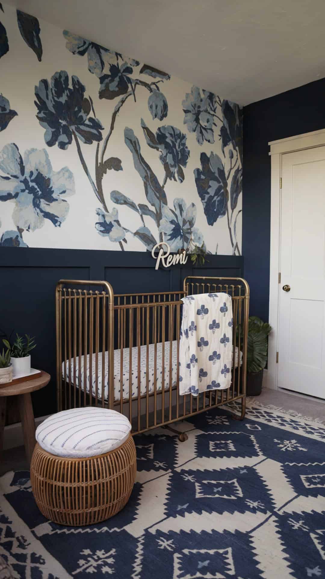 Navy and white nursery with bold floral wallpaper, a gold crib, and rattan pouf, accented by personalized decor.