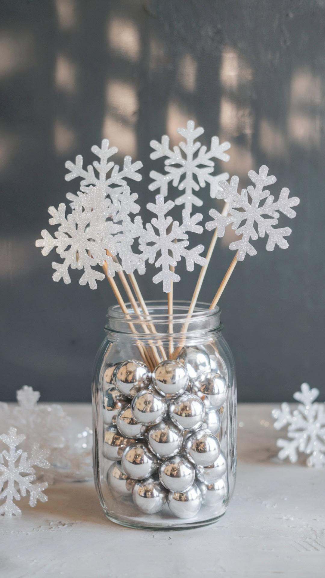 Mason jar filled with silver ornaments and glittery snowflake wands for a winter-themed party centerpiece.