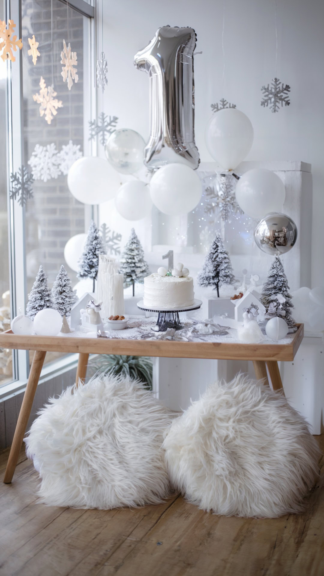 Winter ONEderland dessert table with frosted trees, white balloons, a silver "1" balloon, and a cake centerpiece.